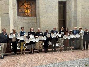 A group of people holding decorated paper plates with handwritten messages in a formal indoor setting.