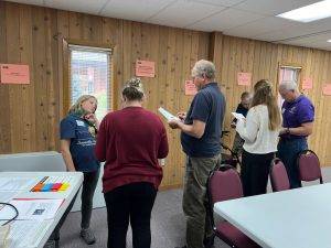 Intergenerational gathering of hunger leaders standing in a semi-circle participating in an interactive hunger simulation.