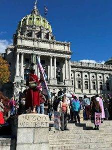 People standing in front of a historic building with a large dome, holding signs.