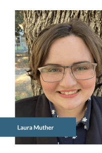 A person with glasses smiles in front of a tree, wearing a navy shirt with white floral patterns and a dark jacket.