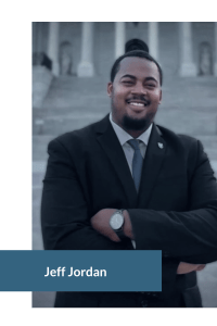 Person in a suit standing in front of stone steps with columns, smiling and arms crossed.